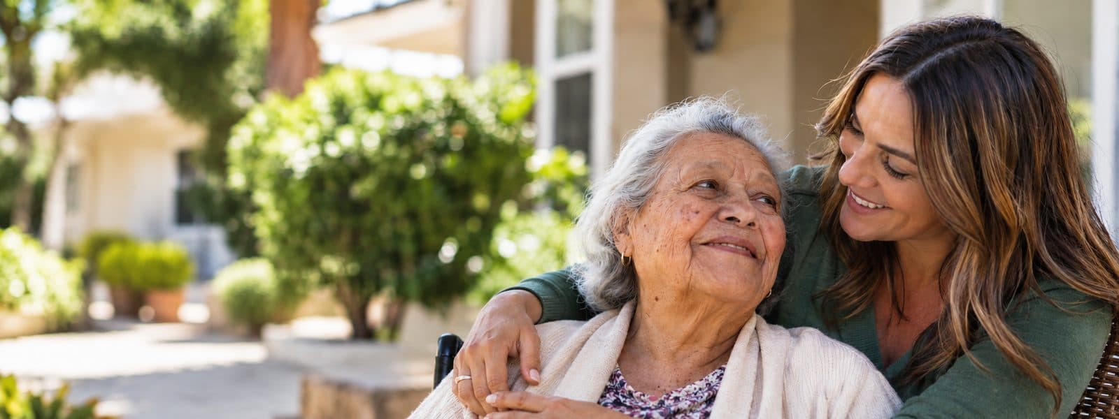 An adult daughter embracing her smiling mother outside a care home